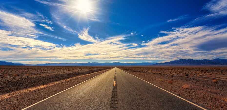 Wide open blue sky with drifts of white clouds and a flat landscape with a road driving off into the distance